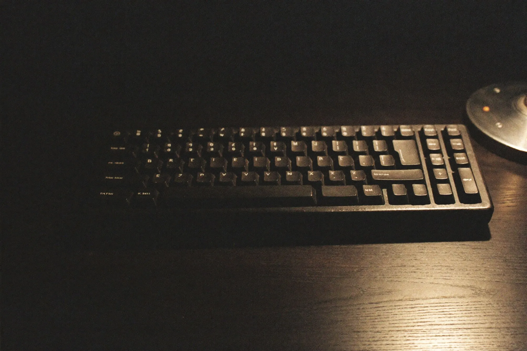 Abgegriffene Tastatur auf dunklem Holz im Licht einer Schreibtischlampe